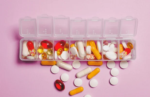 Pillen liegen in Schachteln auf rosa Hintergrund.