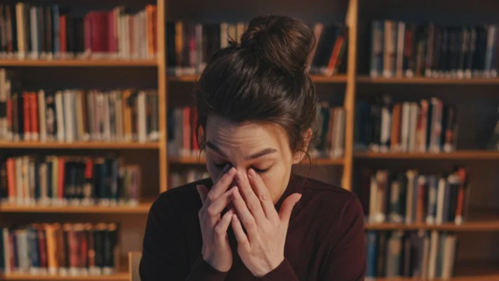 Frau sitzt in der Bücherei und ist müde. Sie reibt sich die Augen.