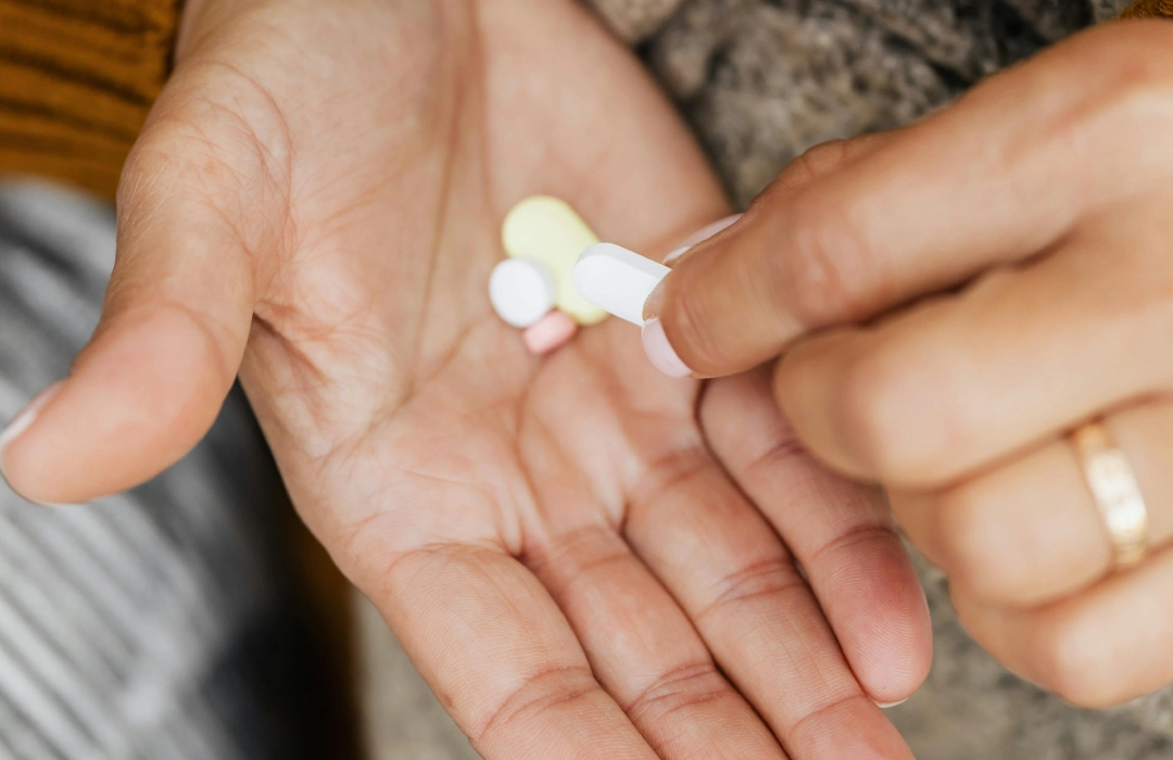 Mehrere Tabletten liegen auf der Hand einer Frau. Mit der anderen Hand nimmt sie eine Tablette.