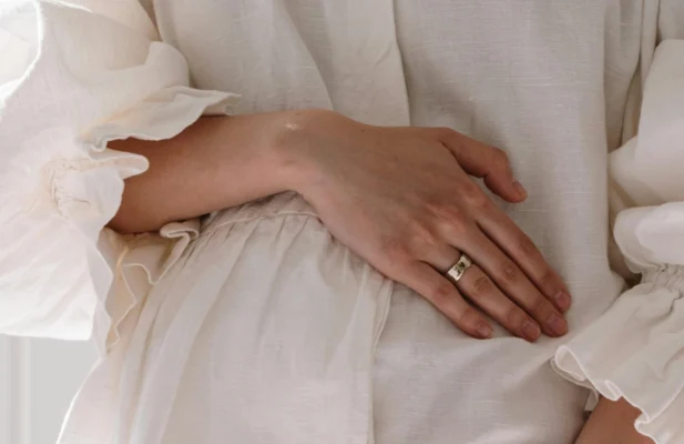 Frau hält Hand auf dem Bauch. Trägt weißes schönes Kleid.