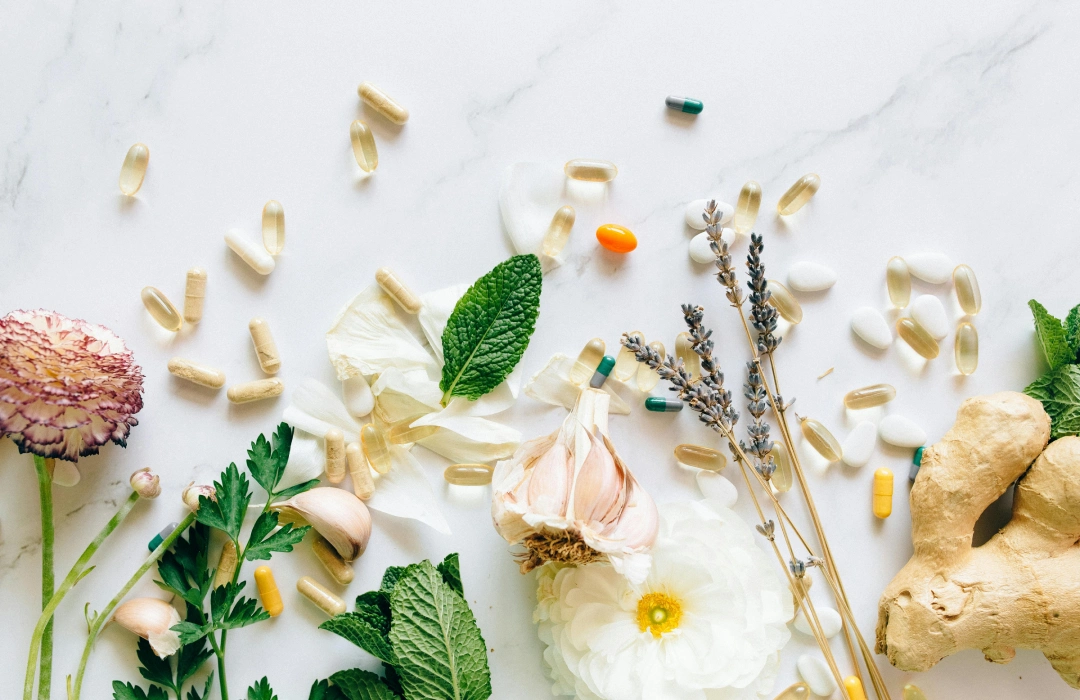 Flatlay Fotografie von Kräutern, Supplements, Ingwer und Blumen auf weißem Marmor.