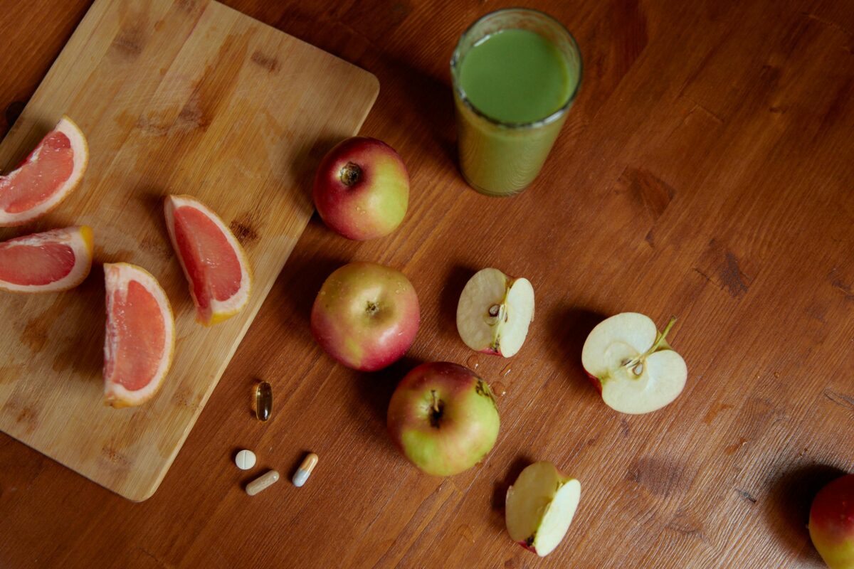 Auf einer Holztischplatte liegen Äpfel, Grapefruit und ein grüner Smoothie.