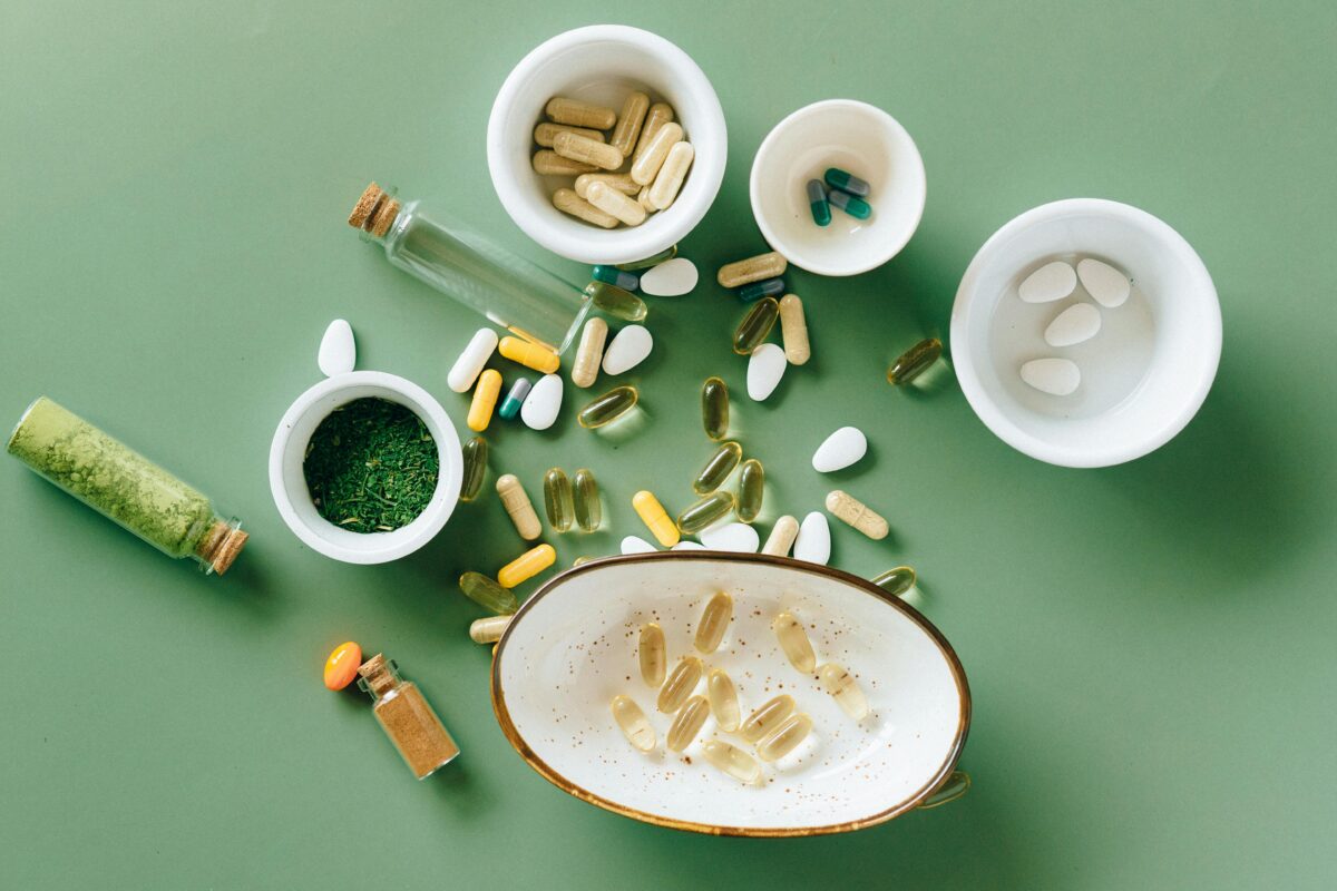 Flatlay Fotografie von vielen Kapseln und Tabletten auf grünem Hintergrund. Viele Schälchen, natürliche vibes.