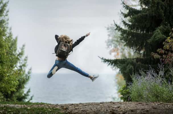 Frau mit Backpack Rucksack springt glücklich während des wanderns.
