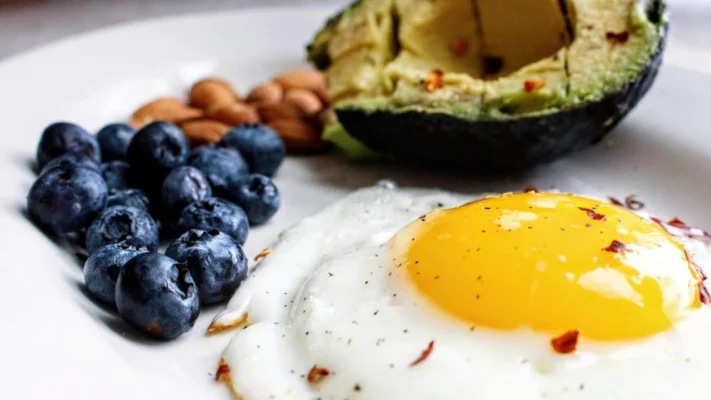 Ein Teller mit gebratenem Ei, Blaubeeren, Mandeln, Avocado. Perfektes ketogenes Frühstück.